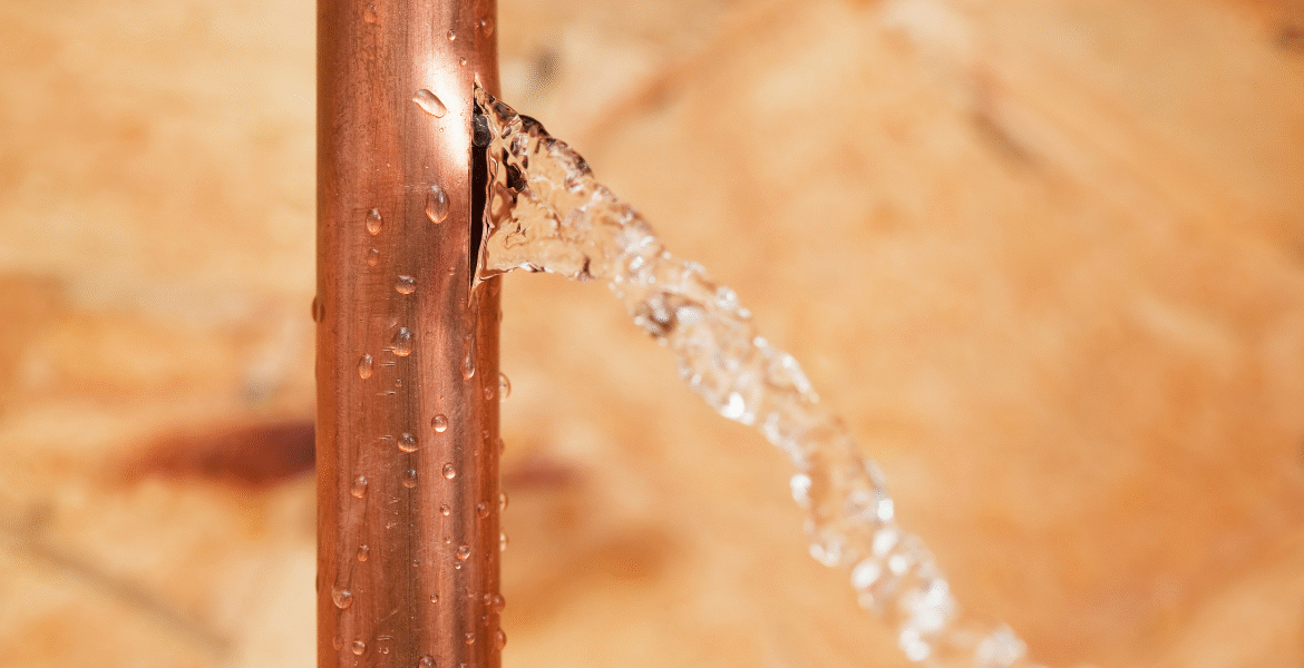 Vertical ac copper pipe leaking water from a crack, with droplets running down the surface, signalling serious damage — air conditioning Gold Coast.