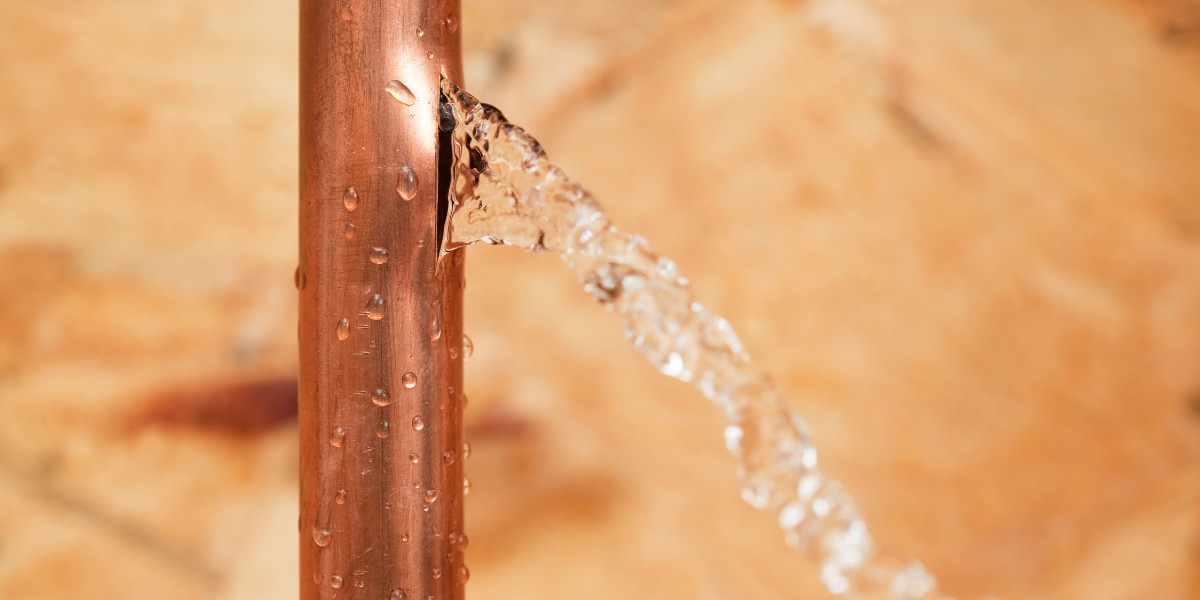 Vertical ac copper pipe leaking water from a crack, with droplets running down the surface, signalling serious damage — air conditioning Gold Coast.