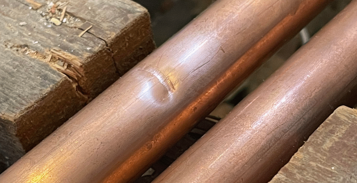 Close-up of a dented copper pipe resting against timber framing, showing a circular impact mark that may affect refrigerant flow in air conditioning Gold Coast systems.