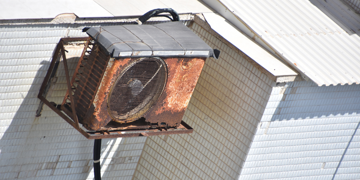Rust-damaged outdoor air conditioner mounted on a building wall, demonstrating long-term corrosion risks without regular servicing to prevent rust in air conditioning Gold Coast.