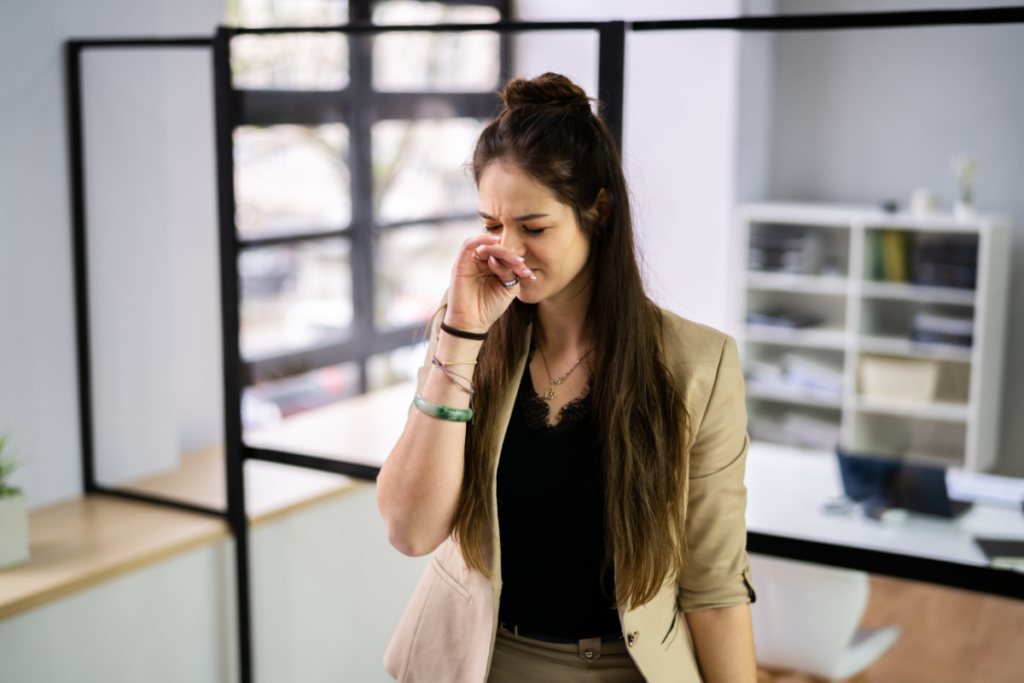 Woman reacting to a burning plastic smell in an office environment, highlighting potential air conditioning issues linked to burning plastic and air conditioning Gold Coast concerns.