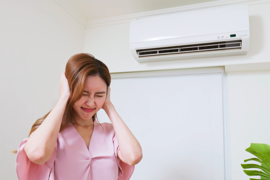 Homeowner covering her ears while standing under a noisy unit, illustrating how air conditioner noise can disrupt comfort in residential air conditioning Gold Coast settings.