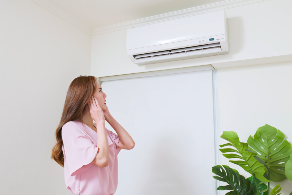 Resident inspecting a wall-mounted AC unit producing unusual air conditioner noise, a common early warning sign in air conditioning Gold Coast environments.