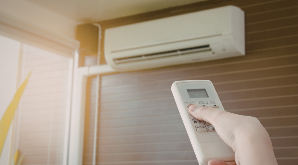 Hand holding remote control adjusting indoor split system – temperature to set air conditioner in fall for comfortable air conditioning Gold Coast homes.