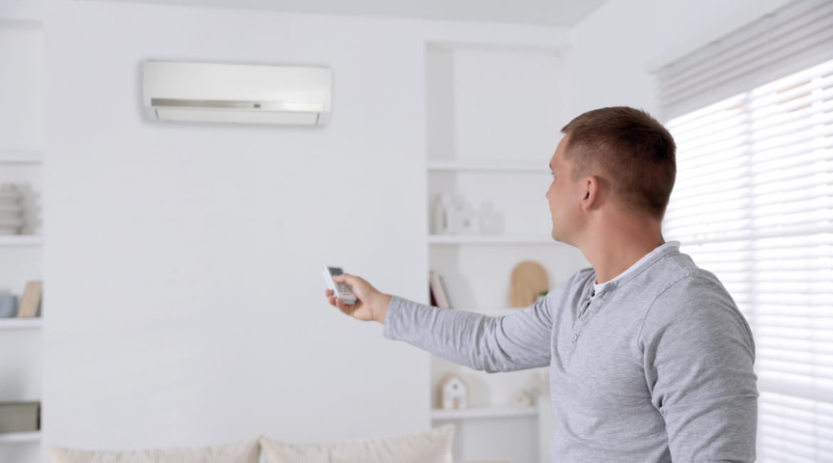 Man using a remote to adjust wall-mounted air conditioner during summer to save power with efficient air conditioning Gold Coast setup.