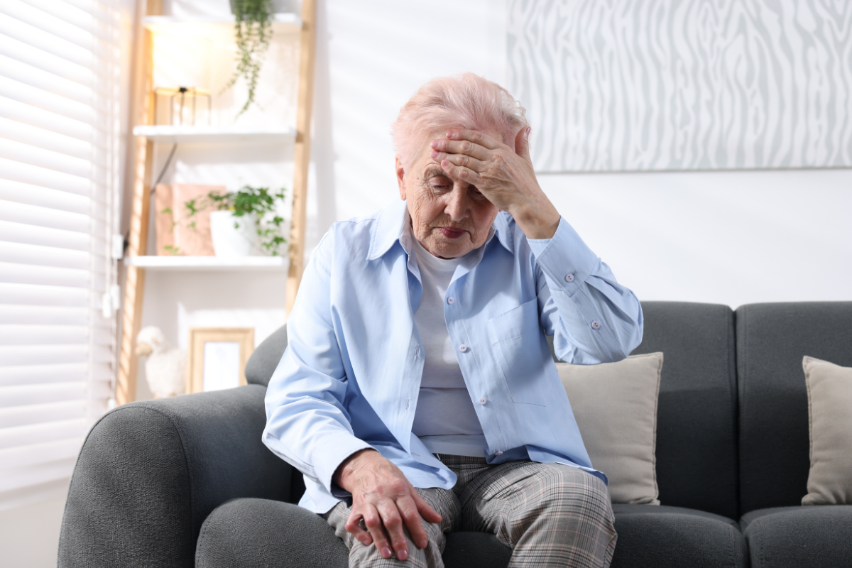 Elderly woman uncomfortable due to stuffier in early autumn conditions, questioning why is my house so hot even when it's cold outside in air conditioning Gold Coast residence.