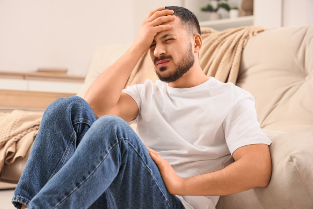 Man sitting on couch feeling headaches from stuffier in early autumn air, exploring what causes a house to feel stuffy in air conditioning Gold Coast home.