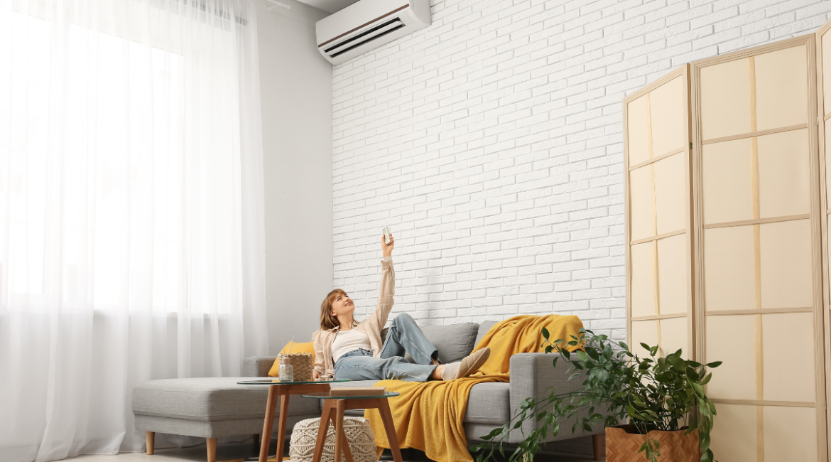 Woman turning off air conditioner with remote in living room, preparing for Turning Off Your Air Conditioner For Fall in Gold Coast climate.