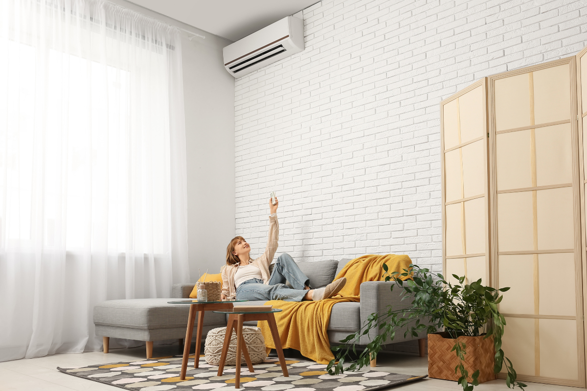 Woman turning off air conditioner with remote in living room, preparing for Turning Off Your Air Conditioner For Fall in Gold Coast climate.