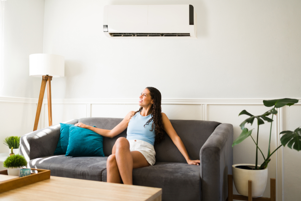 Woman relaxing on sofa under wall-mounted split system, comparing LG vs Panasonic as two of the Best air conditioners in Australia for air conditioning Gold Coast homes, ideal for residential air conditioning Gold Coast comfort.