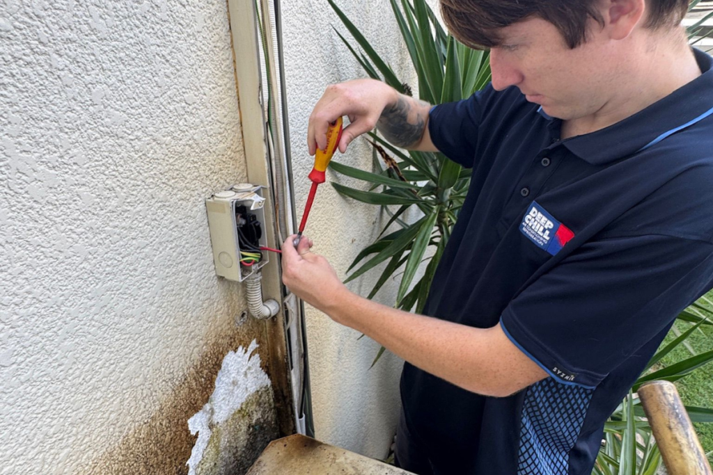 A professional DEEPCHILL technician using a multimeter to test electrical currents on an outdoor unit as part of an air conditioning gold coast safety inspection.