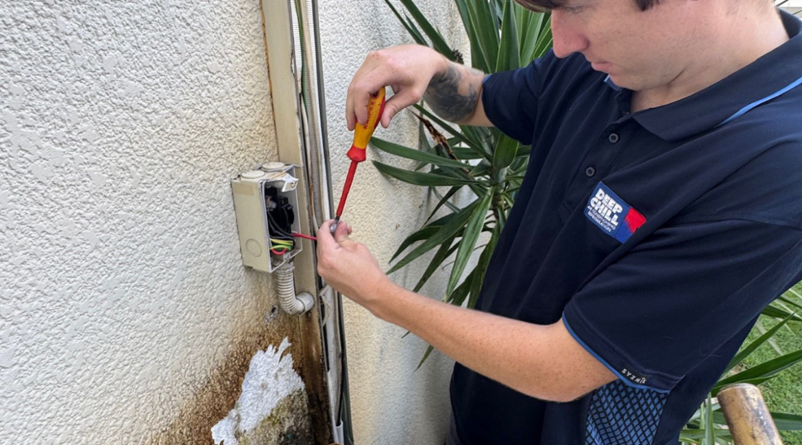 A professional DEEPCHILL technician using a multimeter to test electrical currents on an outdoor unit as part of an air conditioning gold coast safety inspection.