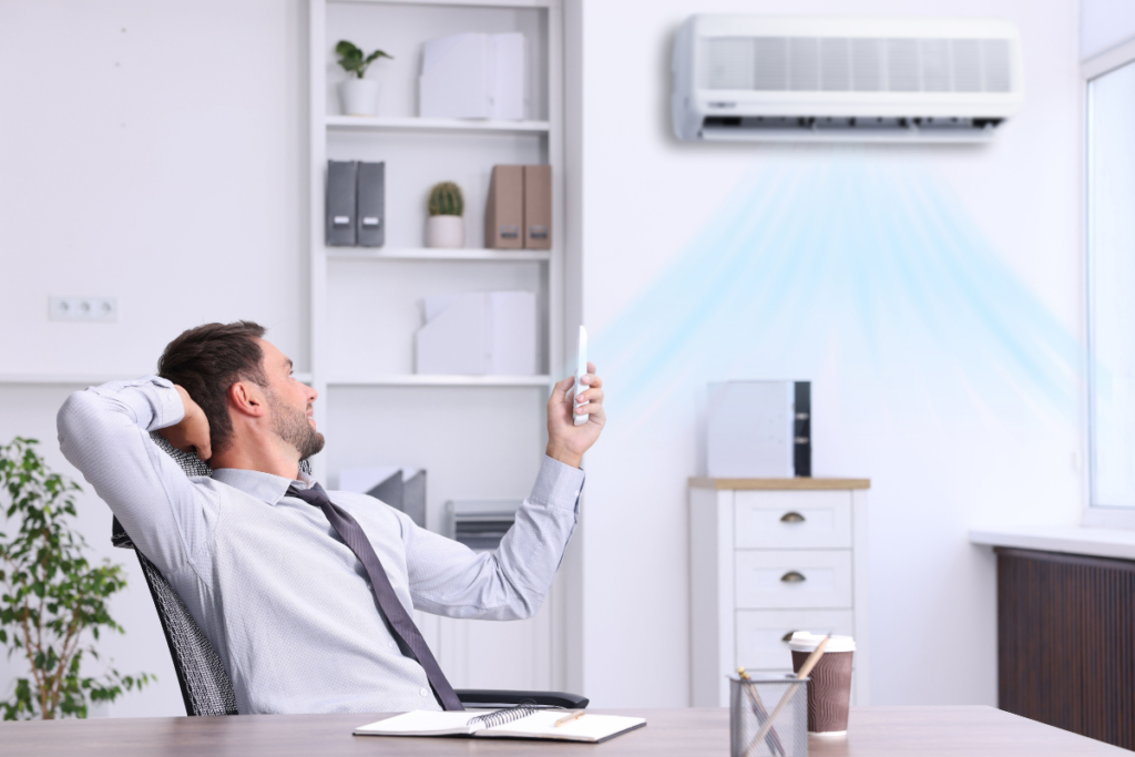 Man relaxing in office chair while using remote to activate AC dry mode, highlighting energy-efficient cooling and humidity reduction for commercial air conditioning Gold Coast environments