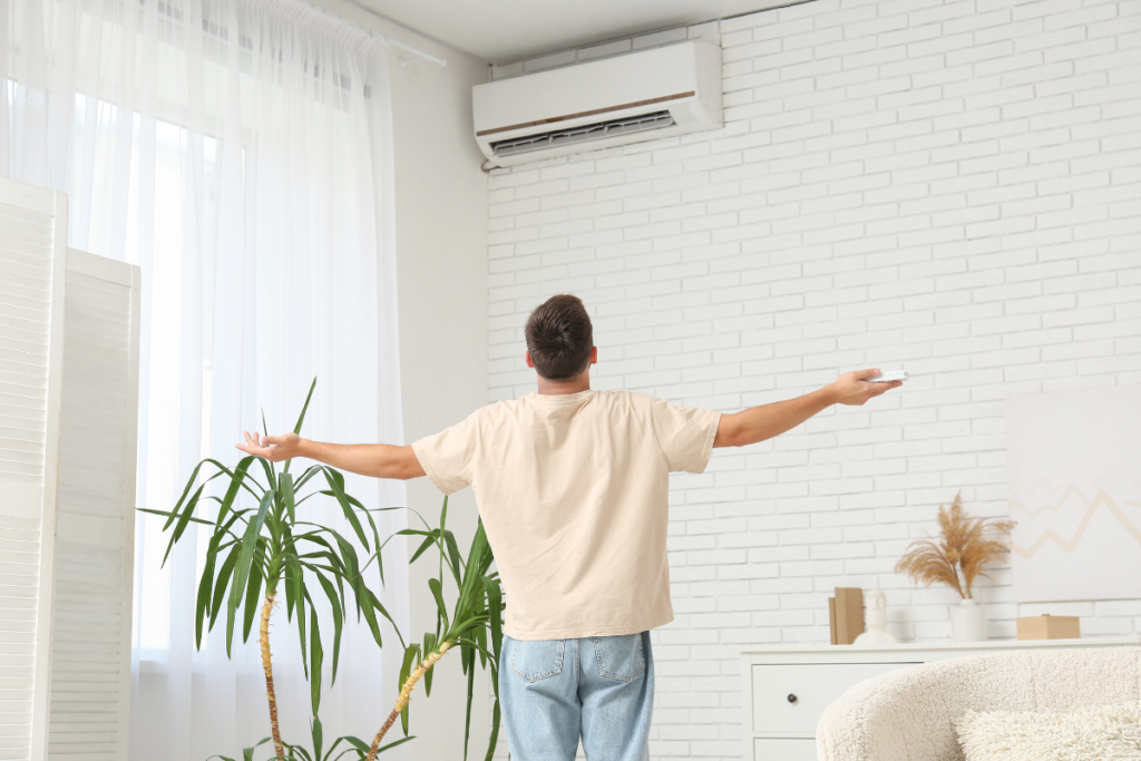 Man standing under wall-mounted air conditioner using remote, demonstrating AC dry mode for better humidity control in residential air conditioning Gold Coast homes, showing if it is cheaper to run AC on dry mode