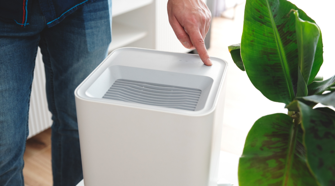 A person presses a button to activate a modern dehumidifier positioned near a tropical banana plant, showing the focused moisture control often need a dehumidifier for special environments, even alongside commercial air conditioning Gold Coast systems.