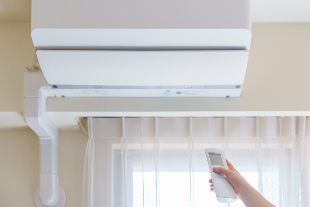 A hand operates a remote control for a wall-mounted residential air conditioning Gold Coast unit with open vents, prompting the question about when you need a dehumidifier.