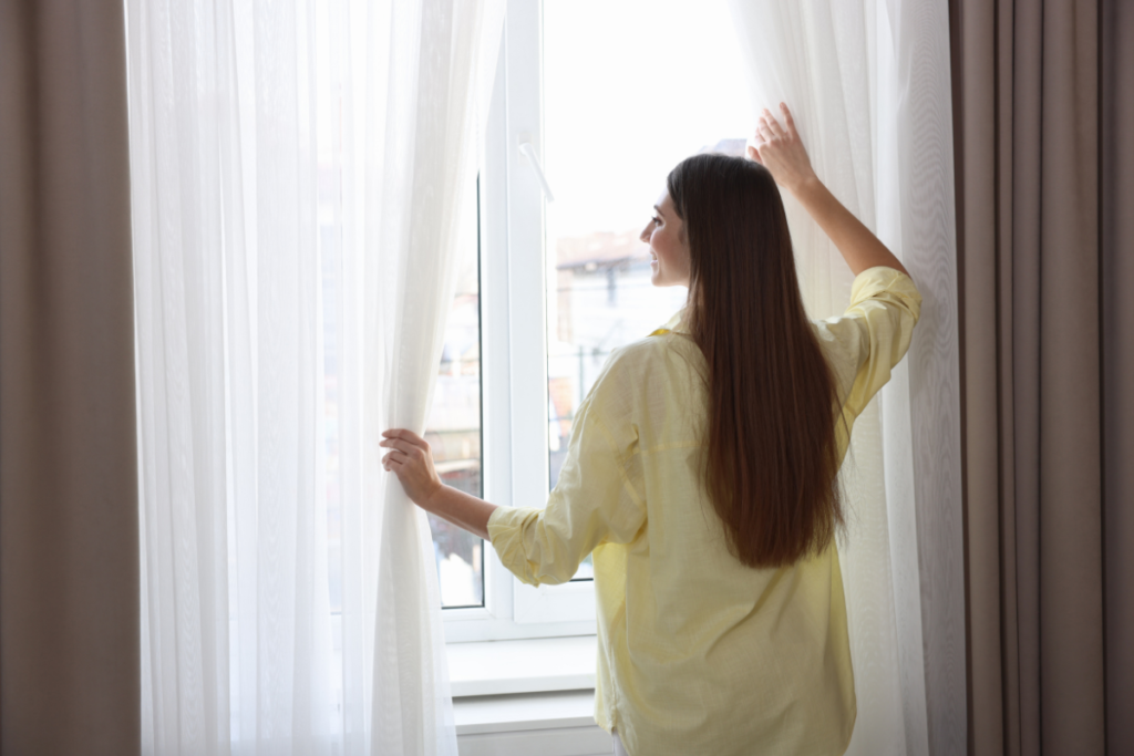 Woman opening curtains and window to let fresh air in, opening the window decrease humidity for commercial air conditioning Gold Coast