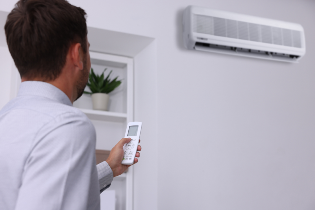 Man using remote to adjust wall-mounted unit, explaining will running my AC reduce humidity and how to make AC remove more humidity for better indoor comfort in air conditioning Gold Coast spaces