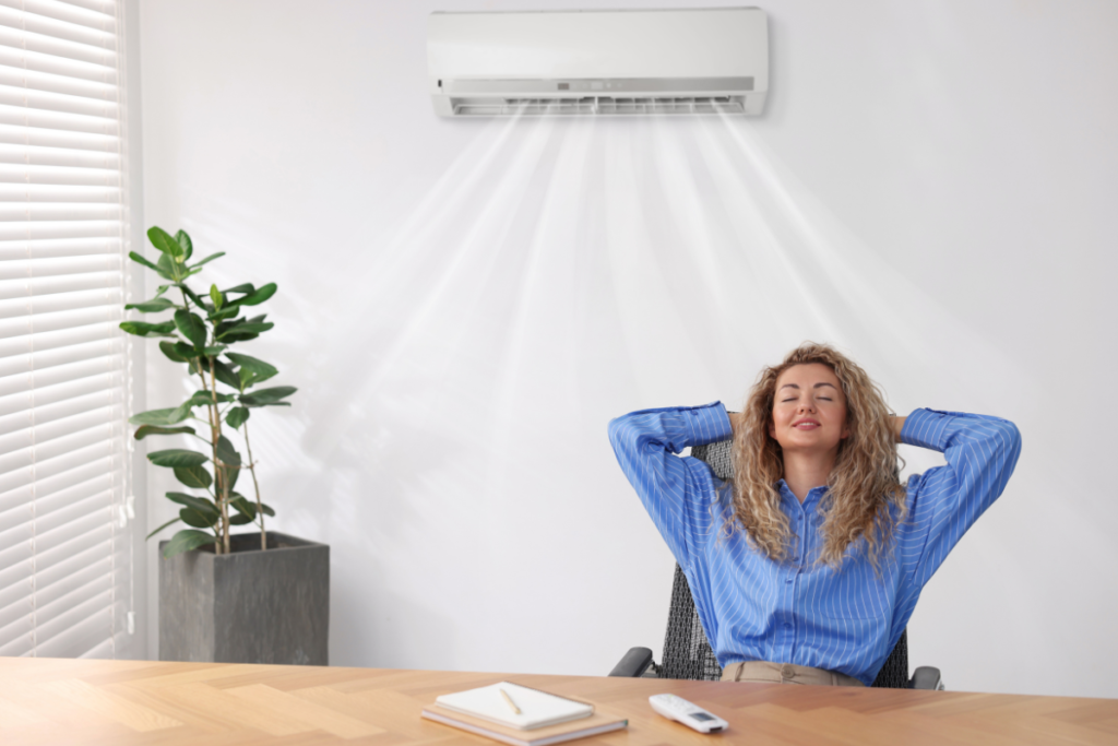 Woman relaxing under wall-mounted air conditioner showing how running your AC will reduce humidity, demonstrating how to make AC remove more humidity in air conditioning Gold Coast homes