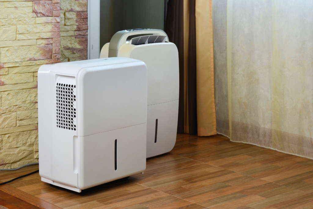 Two portable white dehumidifiers standing on a wooden floor, ideal for larger homes or commercial air conditioning Gold Coast spaces that use a dehumidifier to prevent mold.