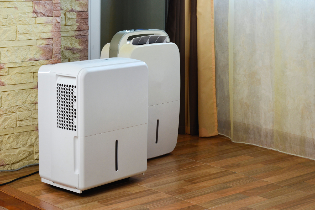 Two portable white dehumidifiers standing on a wooden floor, ideal for larger homes or commercial air conditioning Gold Coast spaces that use a dehumidifier to prevent mold.