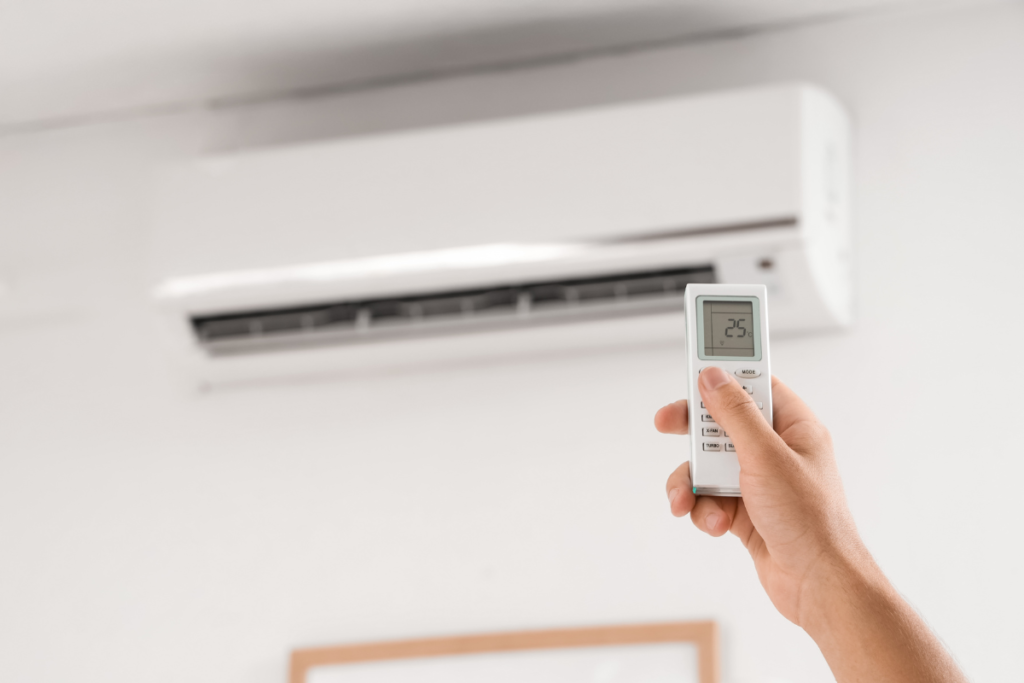 A person using a remote to adjust a white wall-mounted unit, showcasing how AI air conditioning technology simplifies smart home climate control with precision temperature settings.