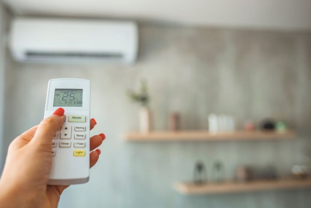 A hand using a remote control to adjust indoor temperature, showing how proper settings prevent air conditioning Gold Coast systems from making the air too dry.