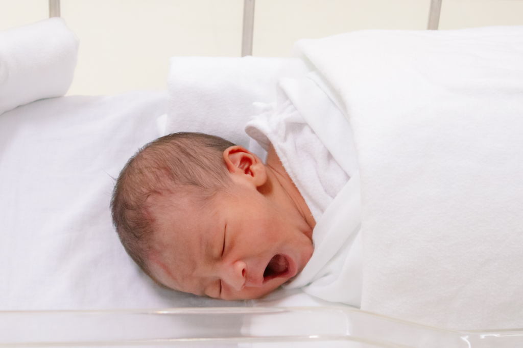 A cute newborn yawning in a clinic bassinet, where safe temperatures are ensured by reliable commercial air conditioning Gold Coast experts.