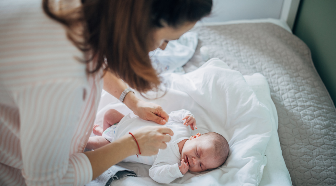 A mother gently dressing her newborn on a bed in a cool, comfortable home maintained by trusted residential air conditioning Gold Coast services.