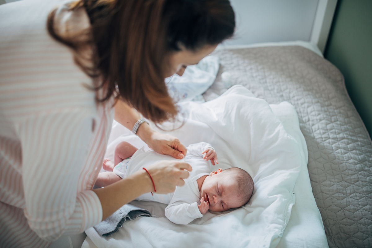 A mother gently dressing her newborn on a bed in a cool, comfortable home maintained by trusted residential air conditioning Gold Coast services.