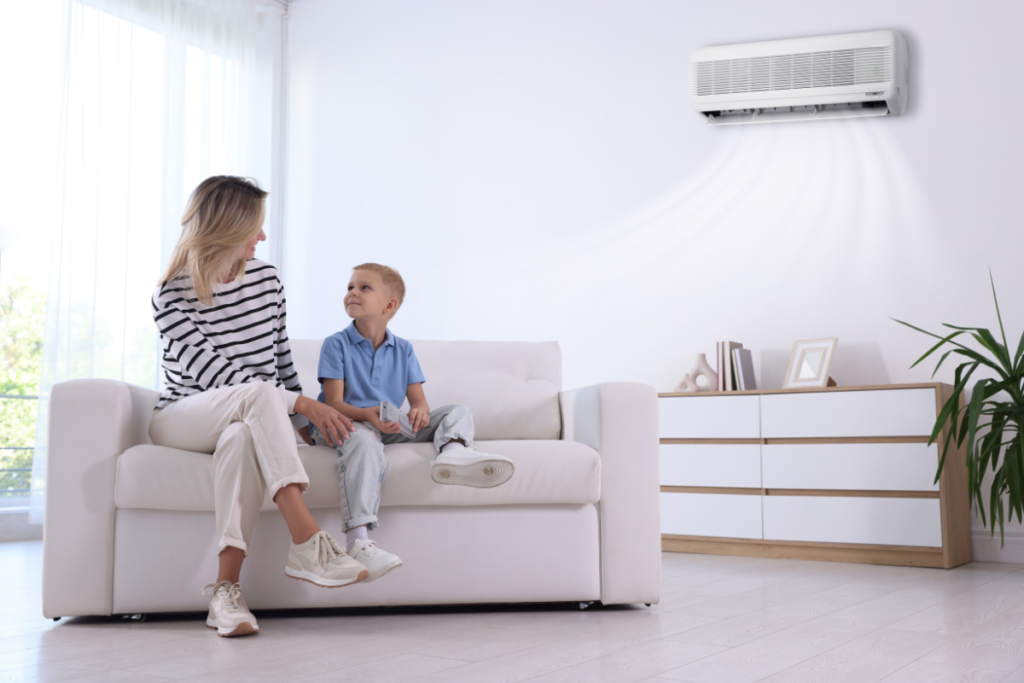 A mother and son relaxing on a white sofa in a modern, sunlit Gold Coast living room, with a modern air conditioner running efficiently on the wall above. They may consider placing a bowl of water in their AC room to improve comfort provided by residential air conditioning gold coast.