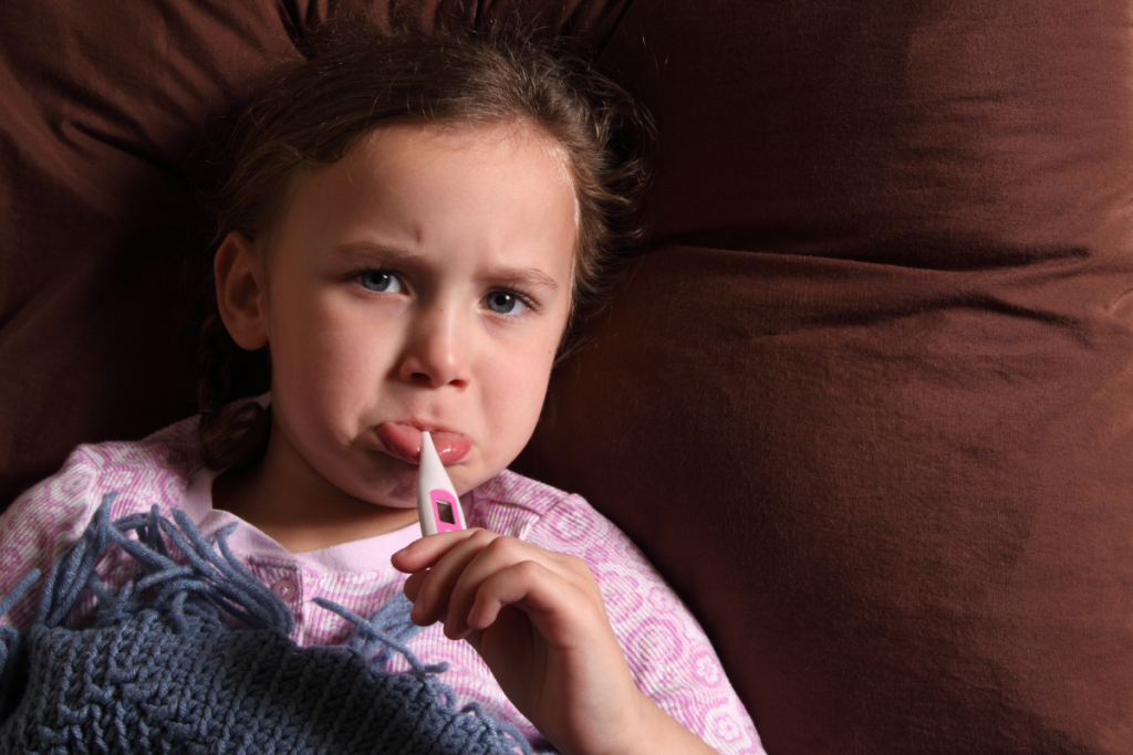 A sick little girl with a fever holding a digital thermometer in her mouth, making parents wonder: is an air conditioner good for a fever?