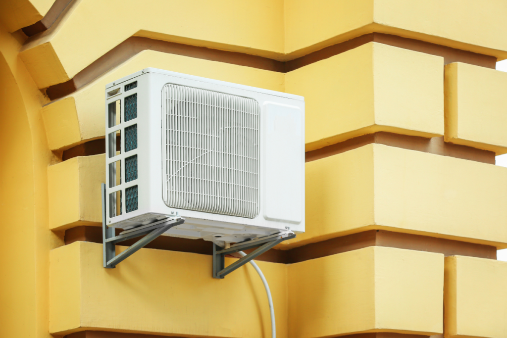 A white Daikin outdoor unit mounted on a yellow textured wall, demonstrating a high-quality residential air conditioning Gold Coast installation capable of Daikin Heat Mode for year-round comfort.