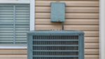 A residential air conditioning condenser unit installed outside a house with beige siding, highlighting the importance of regular air conditioning maintenance gold coast to keep electricity bills low.