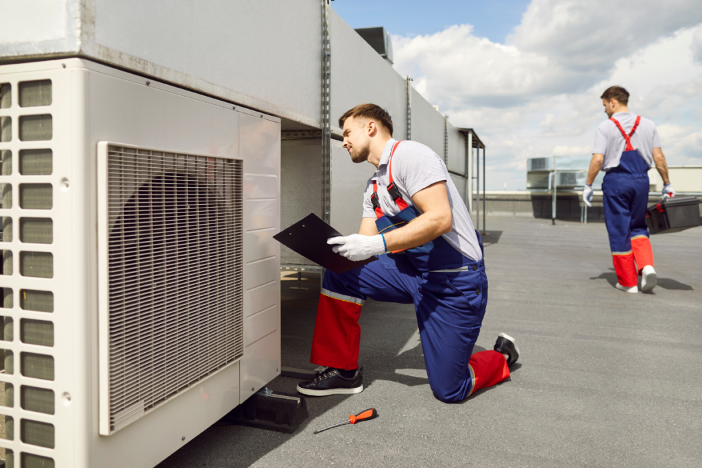 A professional HVAC team performing commercial air conditioning Gold Coast inspections on a rooftop. One technician reviews a checklist while conducting ac maintenance in gold coast on a large outdoor condenser unit.