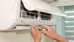 Close-up of a technician's hands using a screwdriver to open a split system for air conditioning maintenance Gold Coast. Regular aircon maintenance helps prevent breakdowns and improves indoor air quality.