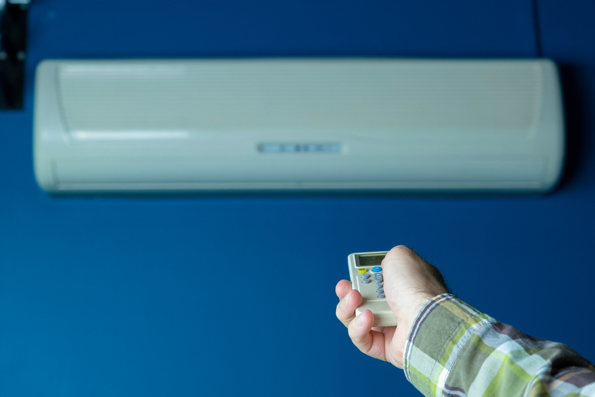 Hand adjusting the temperature for whole house using a remote for an air conditioning Gold Coast unit.