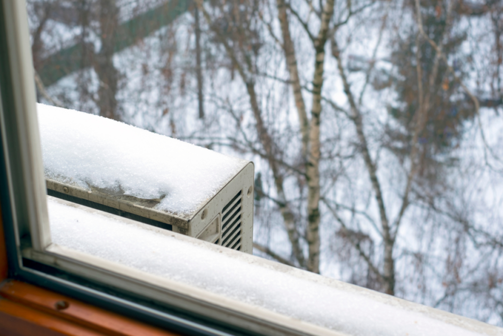 Snow-covered outdoor unit on a window ledge, highlighting issues with maintaining temperature for whole house in extreme weather.