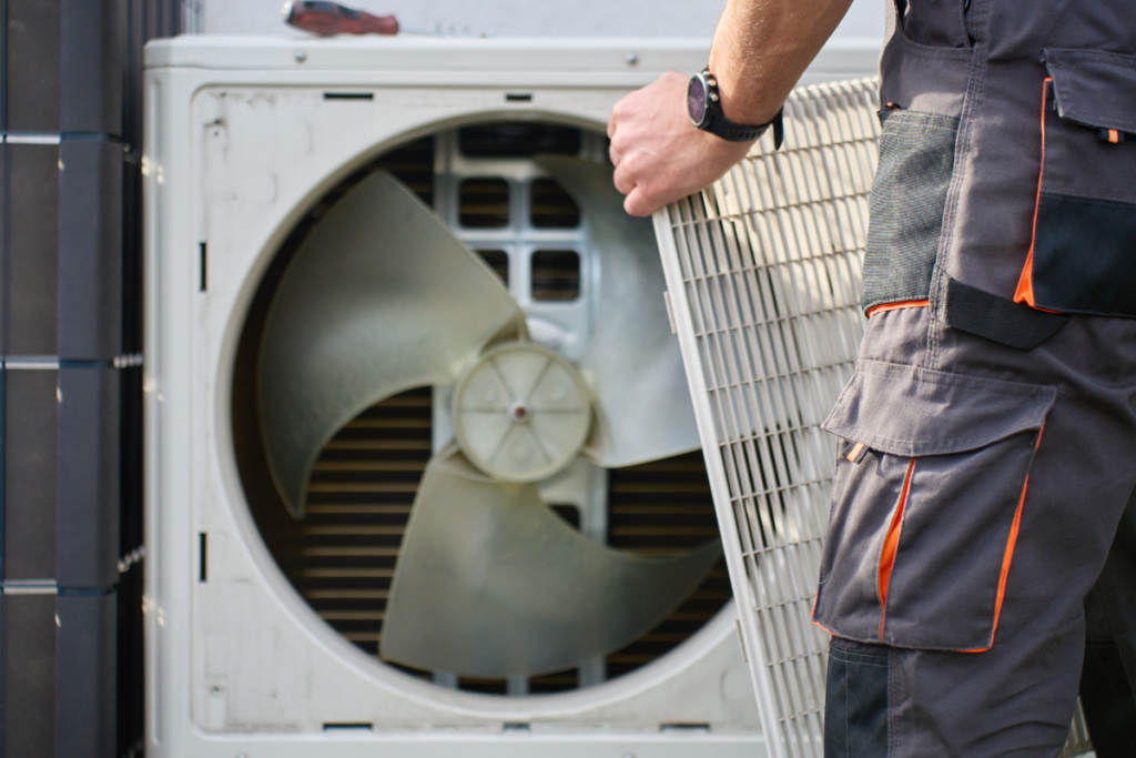 Close-up of an HVAC expert handling an outdoor unit grill, providing expert ac maintenance in gold coast to keep residential air conditioning gold coast systems from blowing white steam.