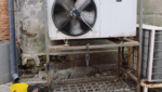 Industrial outdoor HVAC unit with a large spinning fan blade next to a brick wall, an essential commercial setup that needs proactive ac maintenance in gold coast to prevent sudden white steam or failures.