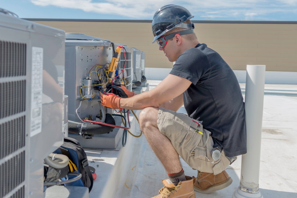 Commercial HVAC technician testing electrical components inside a rooftop air conditioning unit as part of preventative maintenance, reducing the need for emergency commercial air conditioning repair on the Gold Coast.