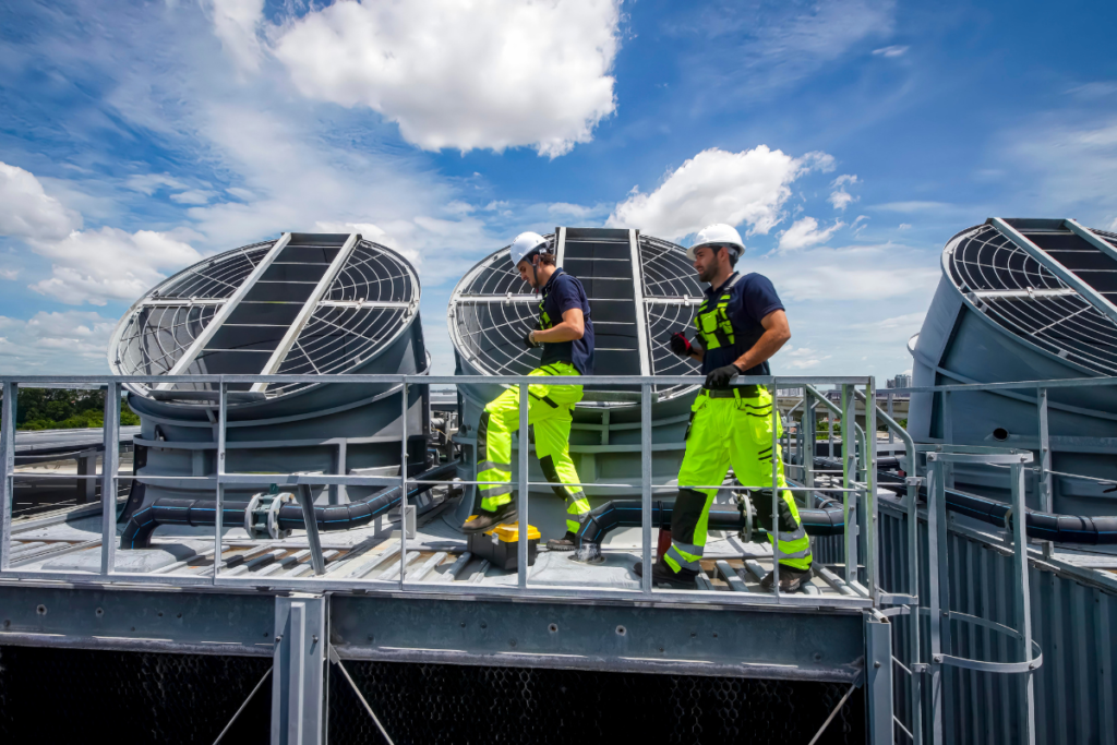 Two technicians on a commercial roof performing regular HVAC maintenance on large cooling towers.