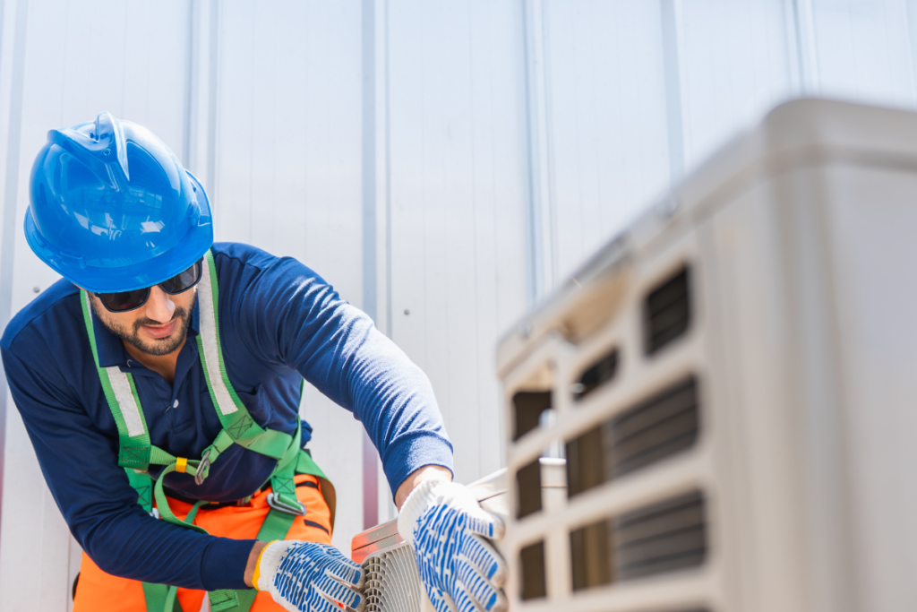 Professional technician in a safety harness inspecting an outdoor condenser unit for commercial air conditioning repair Gold Coast.