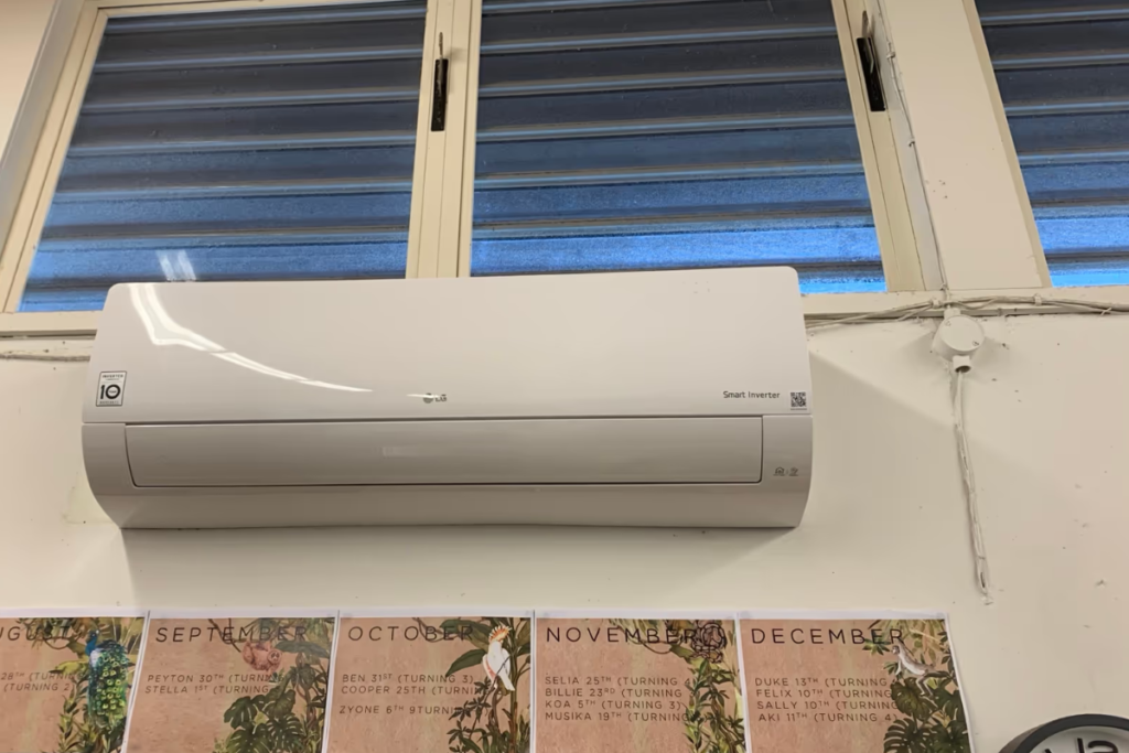 Silver LG Smart Inverter split system above the windows and wall posters, the model behind many a great LG air conditioner review.