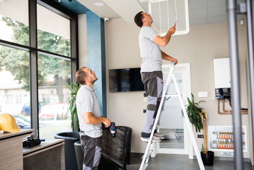 Two technicians installing a ducted air conditioning unit in a Gold Coast office ceiling
