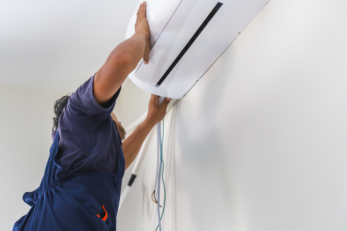 Technician securing an indoor split system air conditioner to the wall, with refrigerant piping visible
