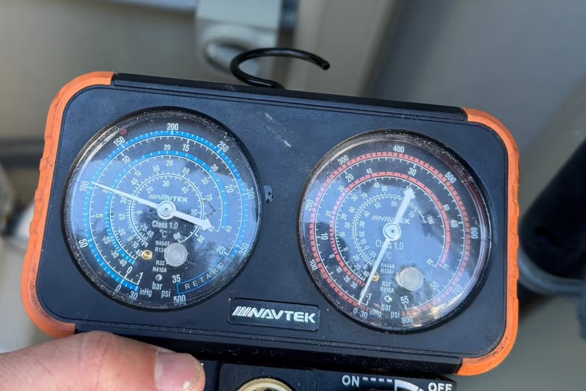 Technician holding NAVTEK gauges reading low-side and high-side refrigerant pressure