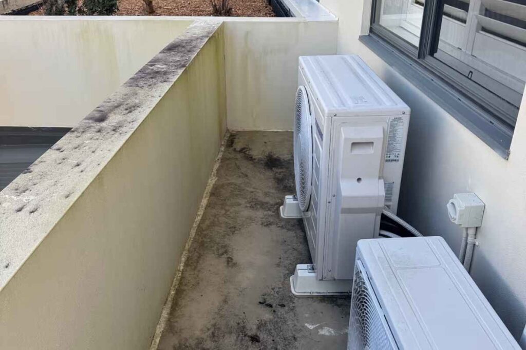 Two outdoor condenser units and a wall isolator on a Gold Coast balcony — an air conditioning Gold Coast setup exposed to rain