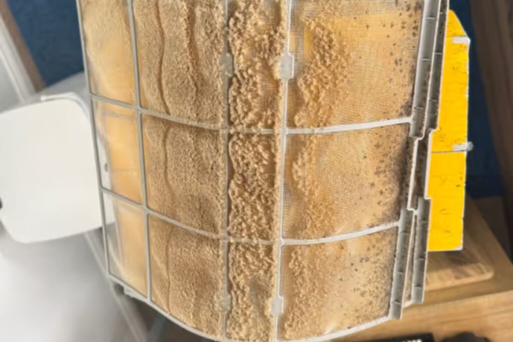 Extremely dirty air filter blocked with dust, highlighting the importance of pre-summer air conditioning service and preventative aircon maintenance.