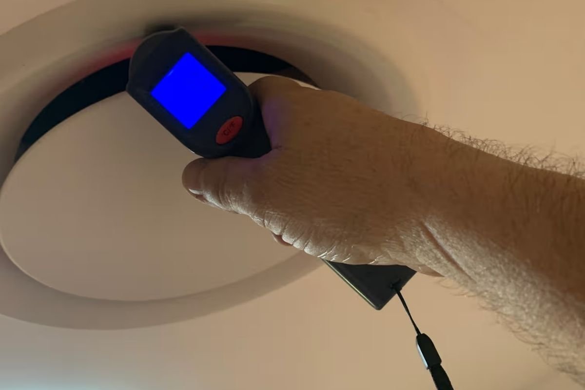 Technician checking a ceiling vent with an infrared thermometer to diagnose weak airflow in one room